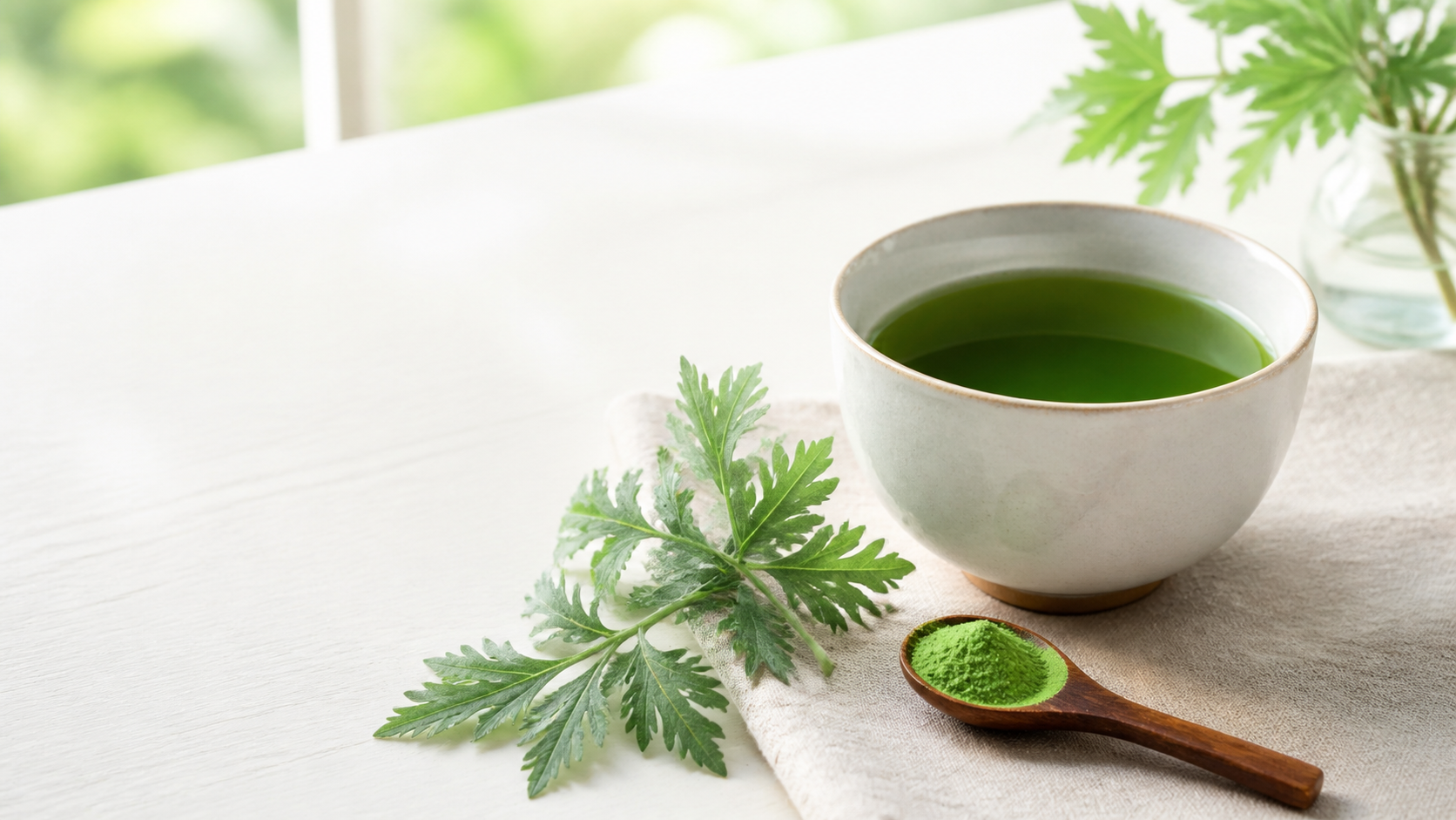 青よもぎ茶とよもぎの葉、パウダーを添えた明るい朝のテーブル